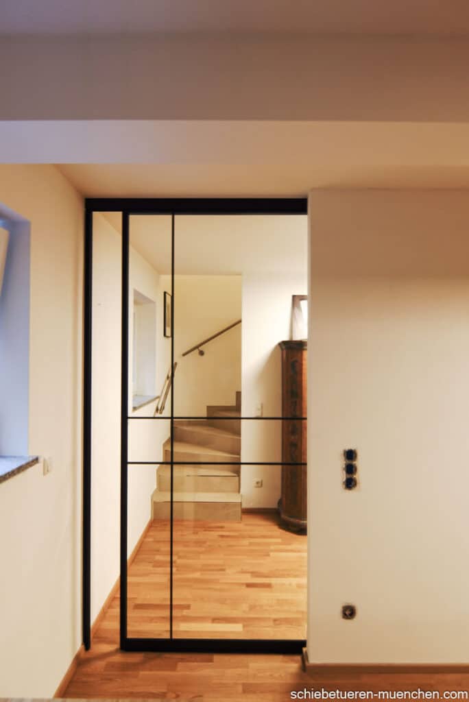 Industrie-Look: Maßgefertigte Schiebetür mit schwarzem Rahmen und Sprossen verschließt einen Durchgang. Door360 München.