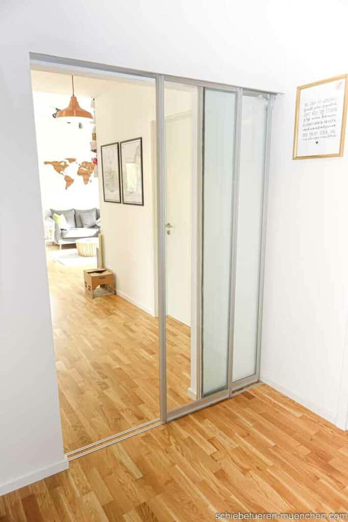 In einer Münchner Wohnung wird ein Durchgang zum Wohnzimmer von zwei Schiebetüren mit Klarglas Füllung verschlossen
