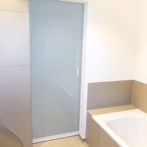 Dichte Milchglas Schiebetür in einem Badezimmer mit weißem Rahmen Stabgriff und Milchglas Füllung