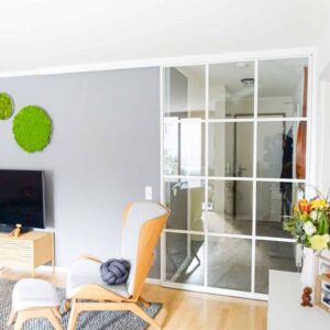 Ein Wohnzimmer wird durch eine große Schiebetüre mit weißem Rahmen und Sprossen vom Flur abgetrennt. Eine individuelle Maßanfertigung von Door360 München