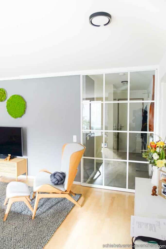 Ein Wohnzimmer wird durch eine große Schiebetüre mit weißem Rahmen und Sprossen vom Flur abgetrennt. Eine individuelle Maßanfertigung von Door360 München