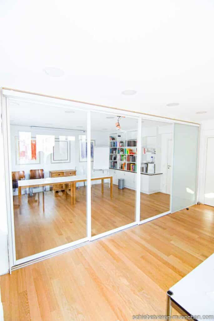 In München kann ein Konferenzzimmer durch Schiebetüren mit Schallhemmglas und einem weißen Rahmen bei Bedarf in zwei separate Räume aufgeteilt werden.