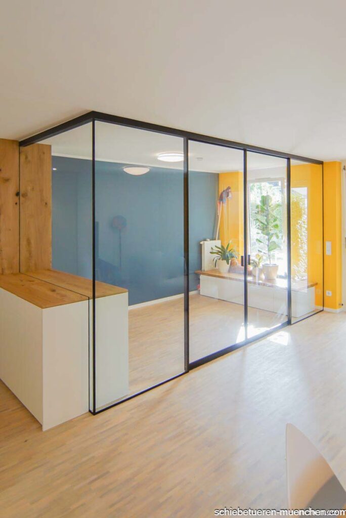 Im Wohnzimmer wurde ein separater Raum für ein Home-Office durch den Einsatz eines Einbauschranks mit Festverglasung und Schiebetüren mit Glasfüllung geschaffen. Der Rahmen der Schiebetüren ist schwarz.