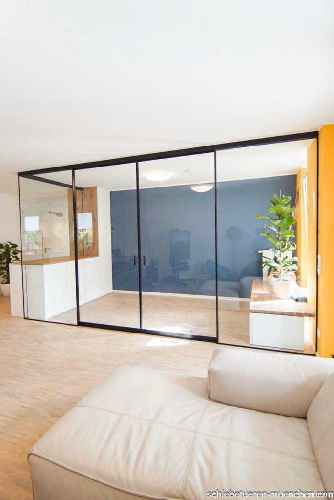 Schaffung eines Home-Office in einem Wohnzimmer durch einen Einbauschrank mit Festverglasung und Schiebetüren mit Glasfüllung. Der Rahmen ist schwarz. Der Raum ist schallgehemmt