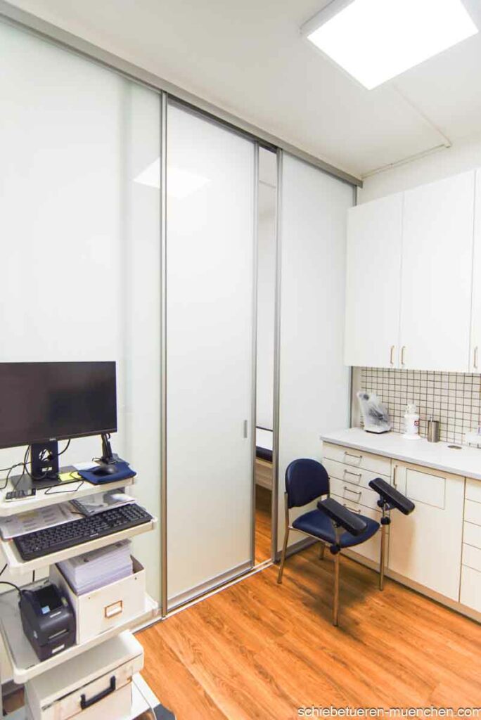 Raumteiler mit raumhohen Schiebetüren zur Abtrennung zweier Behandlungszimmer in einer Altbau-Arztpraxis mit hohen Decken.