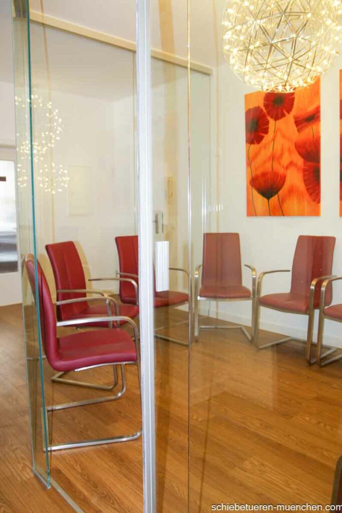 In einer Arztpraxis in München befindet sich ein Glaskubus mit einer Schiebetür, der dazu dient, ein Wartezimmer abzutrennen.
