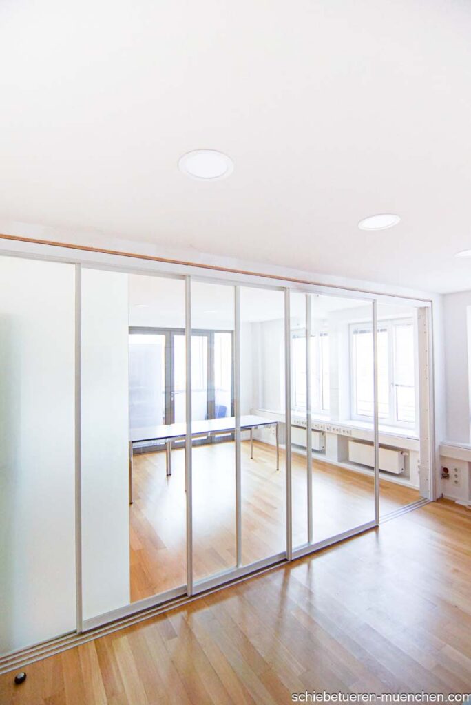 In München kann ein Konferenzraum durch Schiebetüren mit Schallhemmglas und einem weißen Rahmen bei Bedarf in zwei separate Räume verwandelt werden.