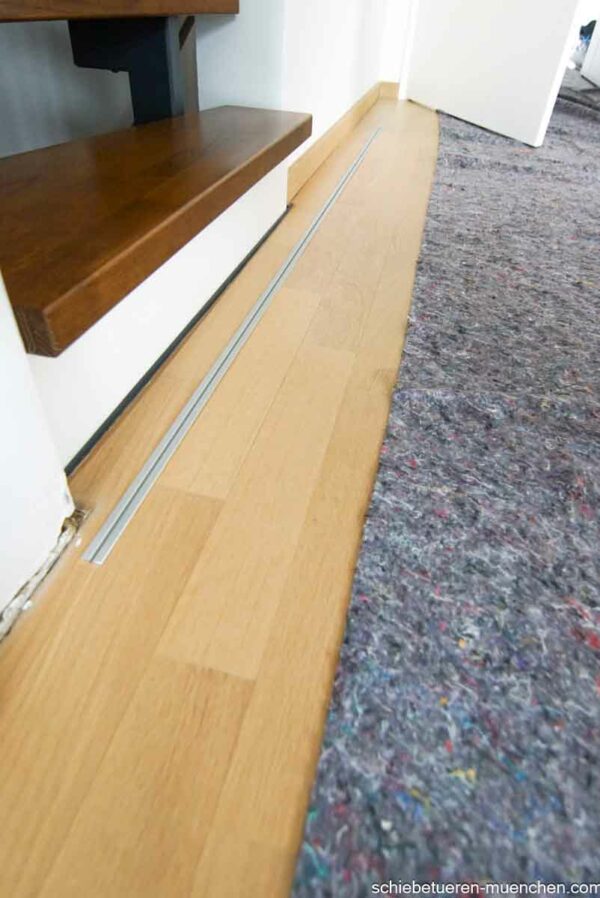 Einflügelige Loft-Schiebetür aus Klarglas mit weißem Rahmen, als elegante Treppenhaus-Abtrennung montiert.