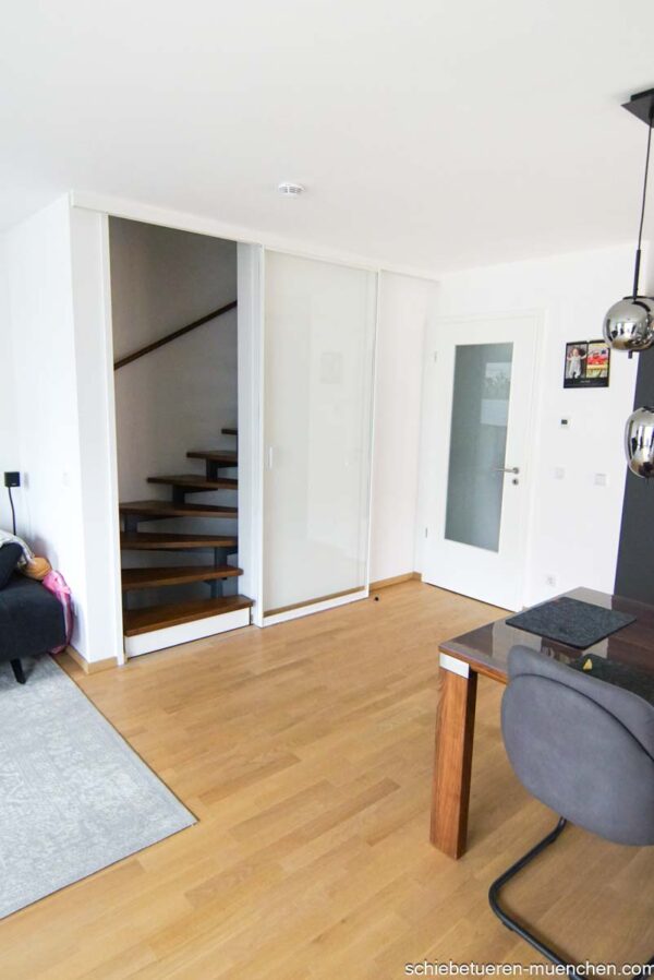 Einflügelige Loft-Schiebetür aus Klarglas mit weißem Rahmen, als elegante Treppenhaus-Abtrennung montiert.