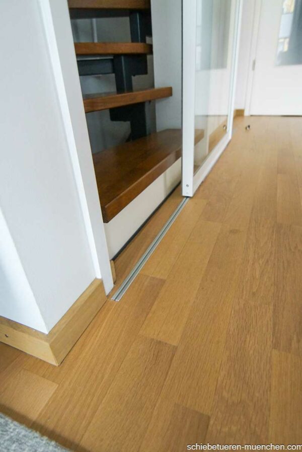 Einflügelige Loft-Schiebetür aus Klarglas mit weißem Rahmen, als elegante Treppenhaus-Abtrennung montiert.