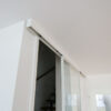 Einflügelige Loft-Schiebetür aus Klarglas mit weißem Rahmen, als elegante Treppenhaus-Abtrennung montiert.