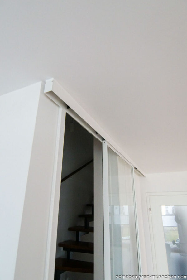 Einflügelige Loft-Schiebetür aus Klarglas mit weißem Rahmen, als elegante Treppenhaus-Abtrennung montiert.