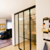 Zweiteilige Loft-Schiebetür mit schwarzem Aluminiumrahmen und Glaseinsätzen im Industrie-Look, als Abtrennung zwischen Treppenhaus und Wohnbereich.