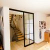 Zweiteilige Loft-Schiebetür mit schwarzem Aluminiumrahmen und Glaseinsätzen im Industrie-Look, als Abtrennung zwischen Treppenhaus und Wohnbereich.