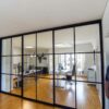 Industriedesign Raumteiler im Büro – deckenmontierte Schiebetüren von door360 mit schwarzen Sprossen.