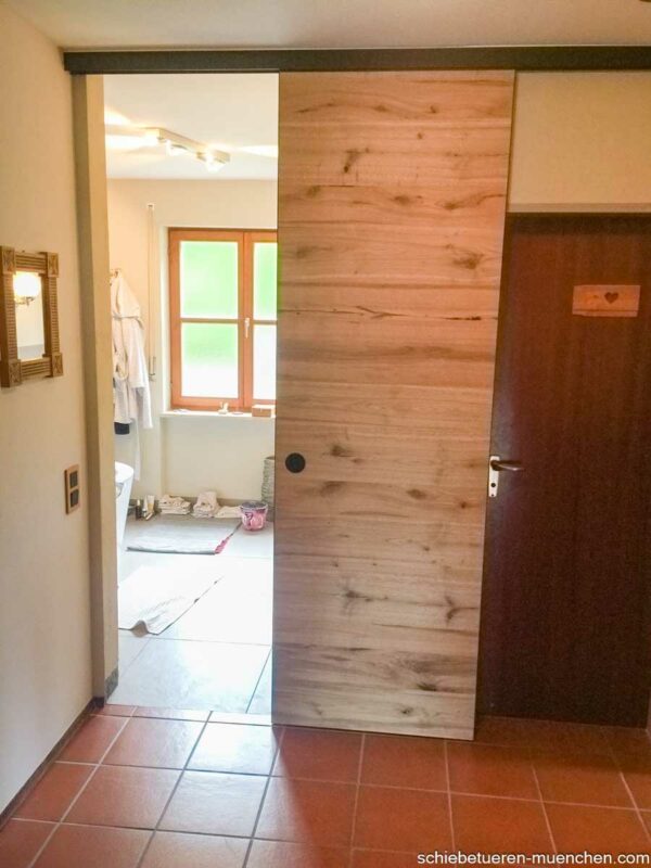 Schiebetür aus Altholz-Eiche im Badezimmer, geöffnet zur Badewanne, Deckenmontage mit schwarzer Laufschiene.