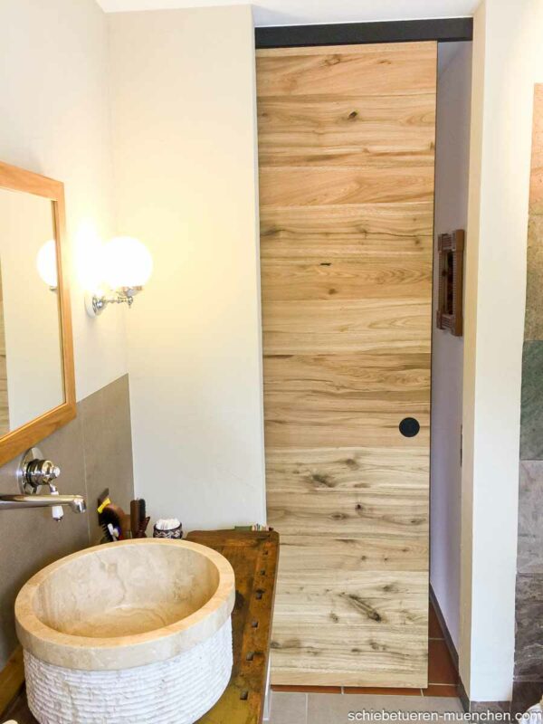 Holz-Schiebetür aus Altholz-Eiche, geschlossen im Badezimmer neben einem Waschtisch mit Natursteinbecken