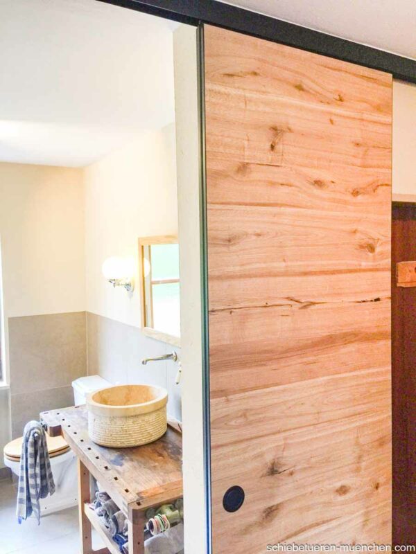 Holz-Schiebetür aus Altholz-Eiche, geschlossen im Badezimmer neben einem Waschtisch mit Natursteinbecken, Deckenmontage.